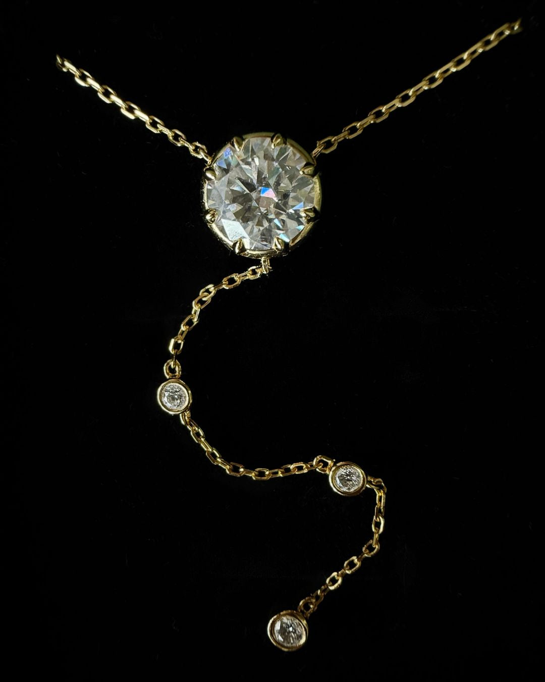 Macro view of the Lumina Drop Necklace with a 3 ct round moissanite center stone and three smaller bezel-set moissanites along the lariat drop.