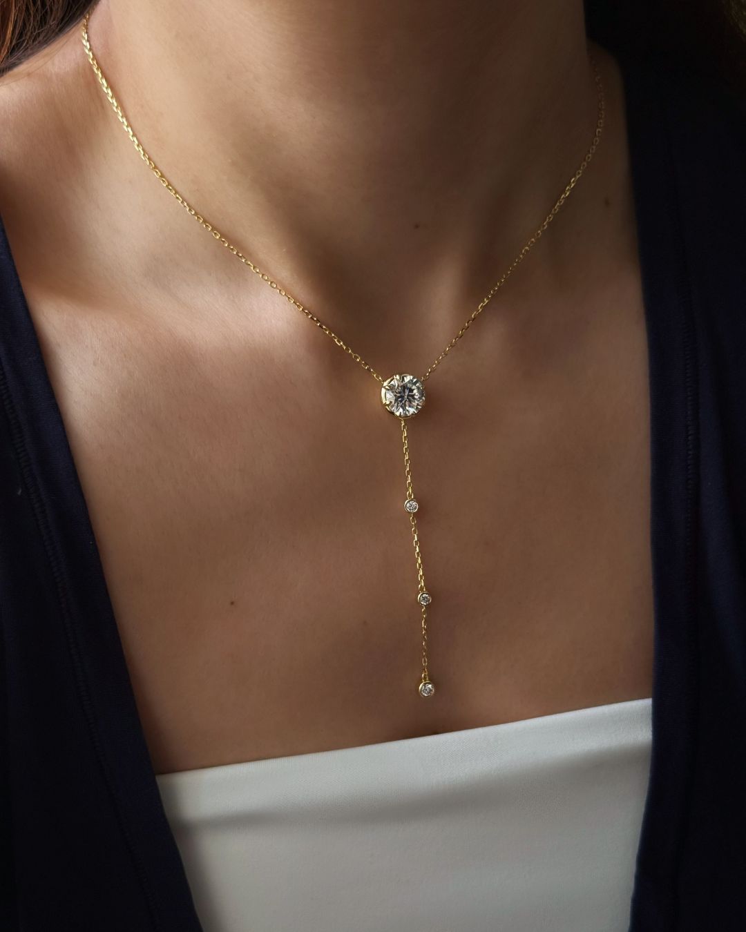 Lumina Drop Necklace worn at the collarbone with a 3 ct round moissanite center stone and delicate gold lariat drop.