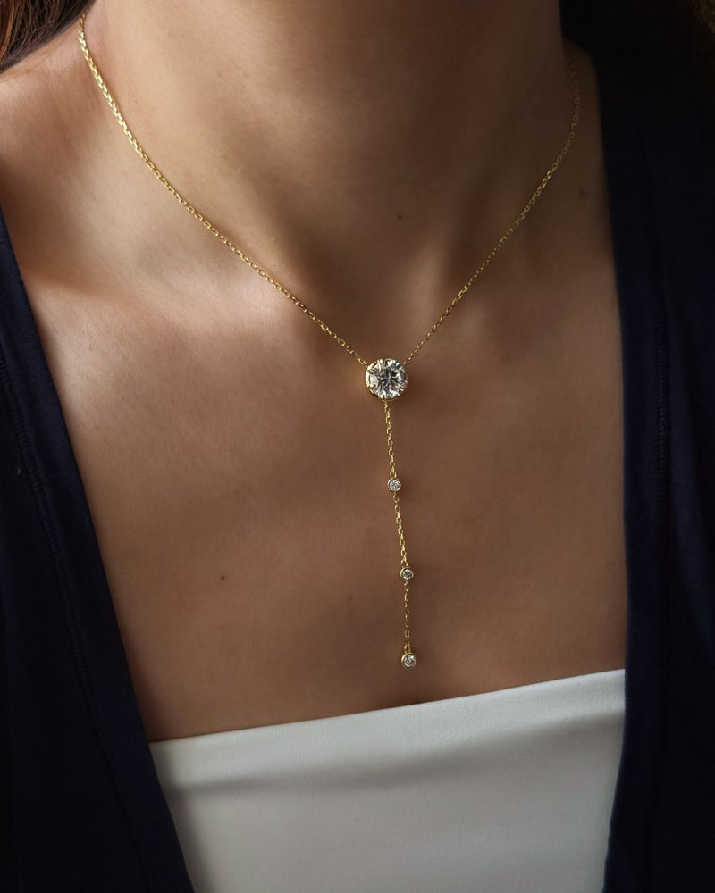 Lumina Drop Necklace worn at the collarbone with a 3 ct round moissanite center stone and delicate gold lariat drop.