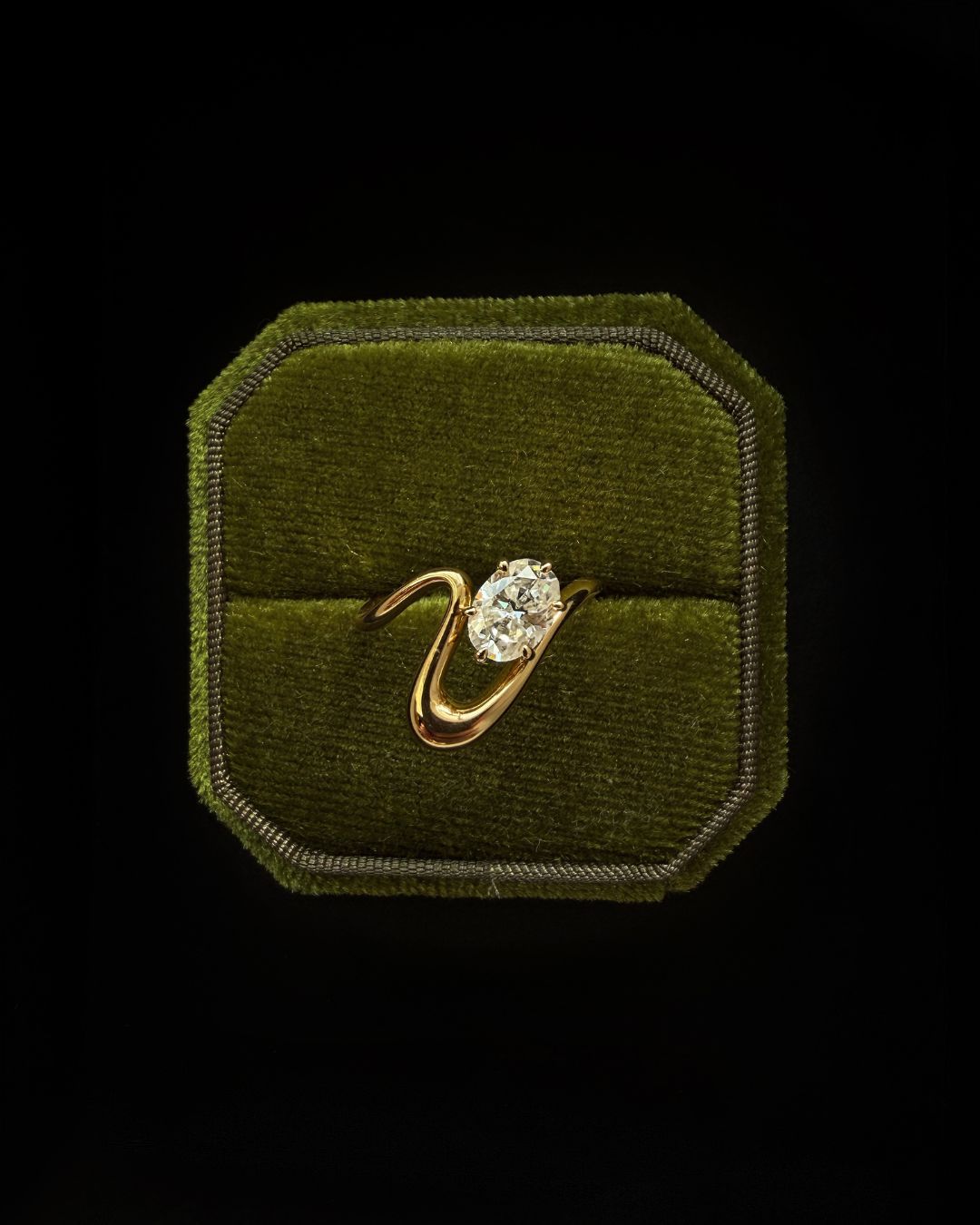 Luxury gold wave band pinky ring with oval moissanite displayed in a textured ring box setting