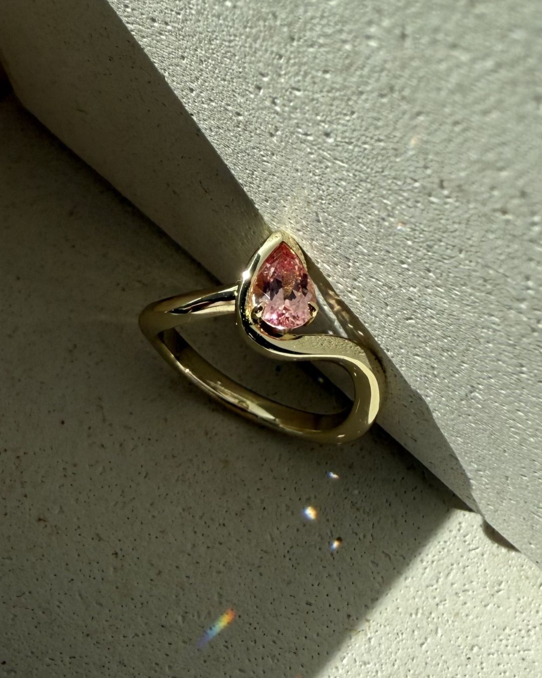 Pear cut pink gemstone ring with sculptural gold band captured in natural light with soft shadows