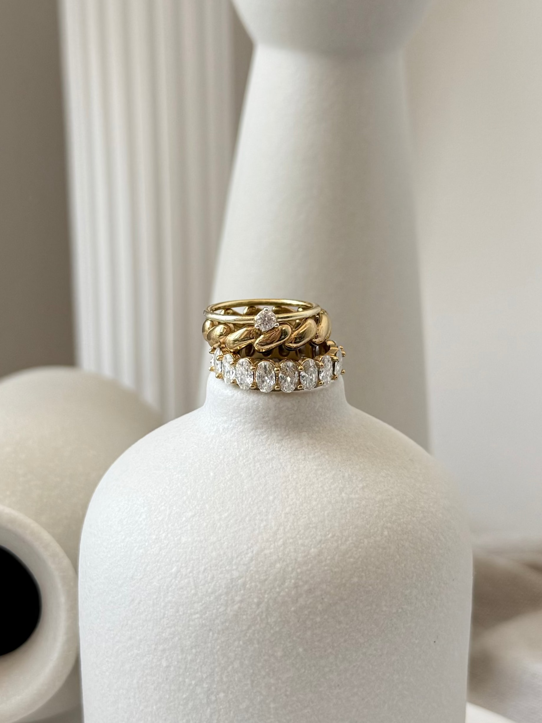 Gold and diamond ring on a white vase with a neutral background