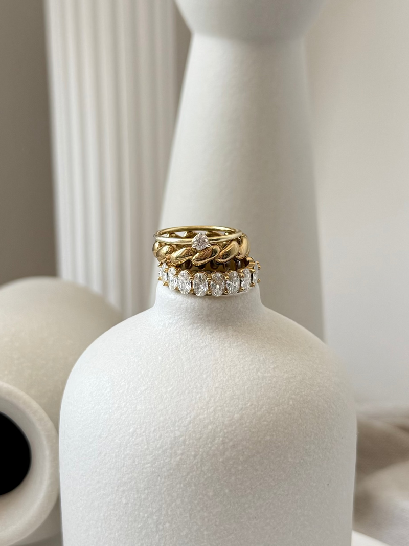 Gold and diamond ring on a white vase with a neutral background