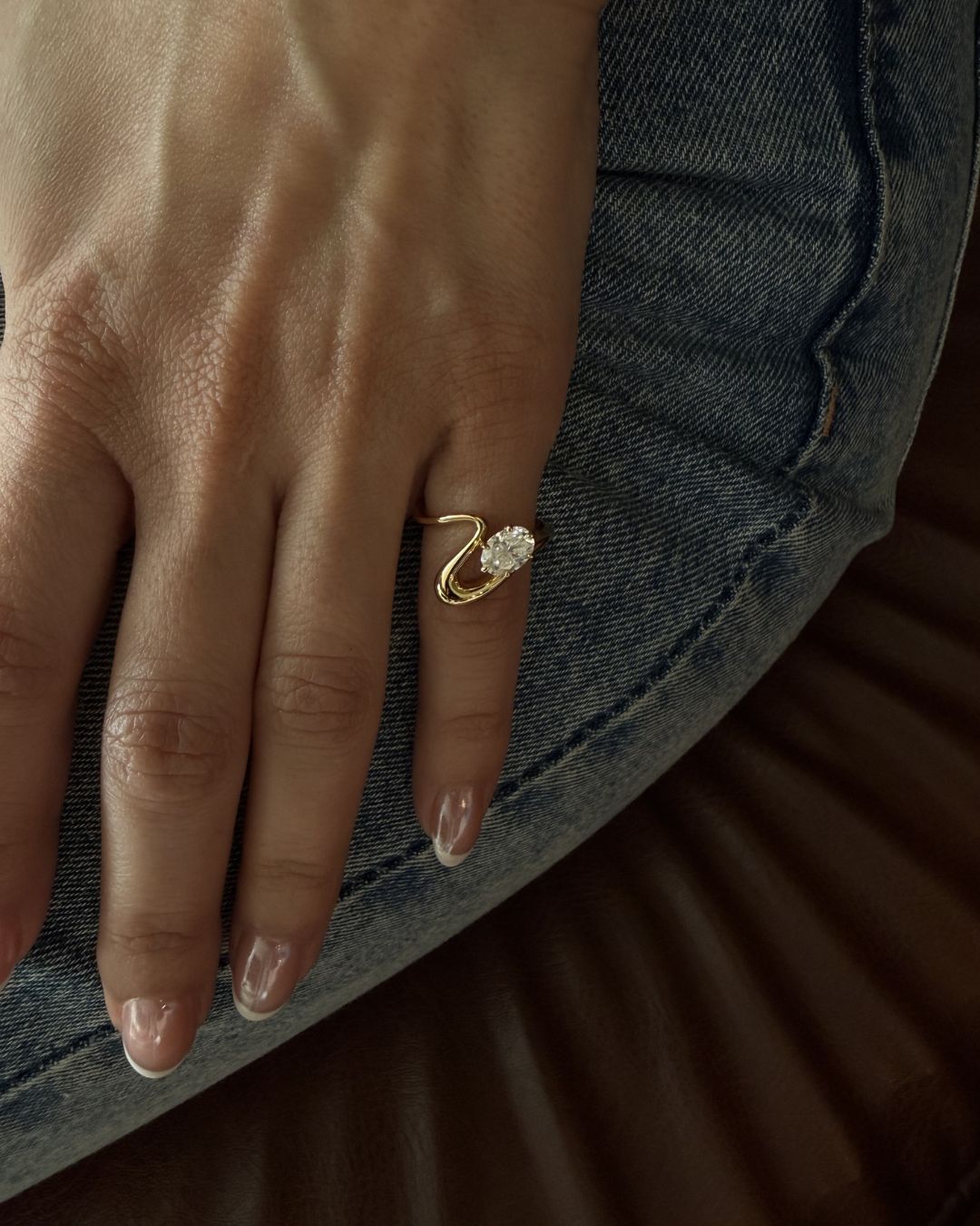 Oval moissanite pinky ring worn on hand with a sculptural curved gold band in natural lighting